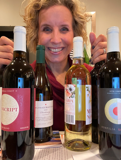 woman smiling with bottles of wine on the table in front of her