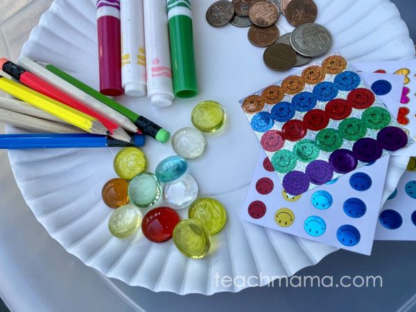 pencils, markers, coins, stickers, and glass beads on a white plate