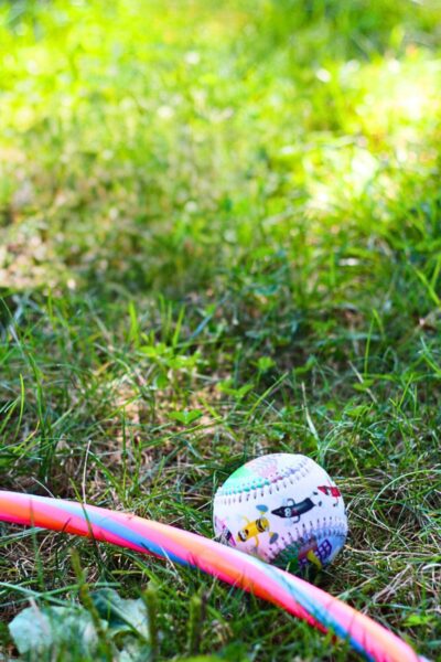Green grass with a red and blue hula hoop and a white soccer ball with blue, green and red colors.
