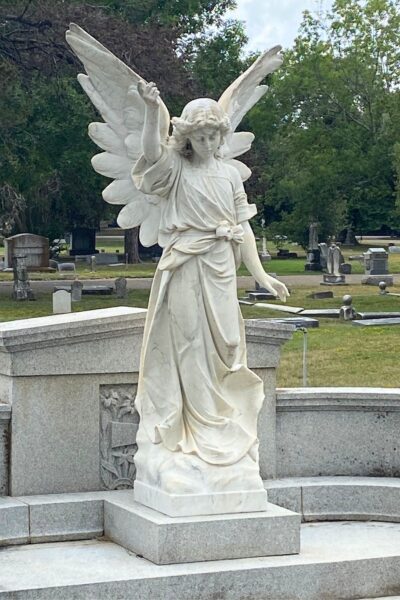 White stone angel with wings and an upraised arm standing in a cemetery