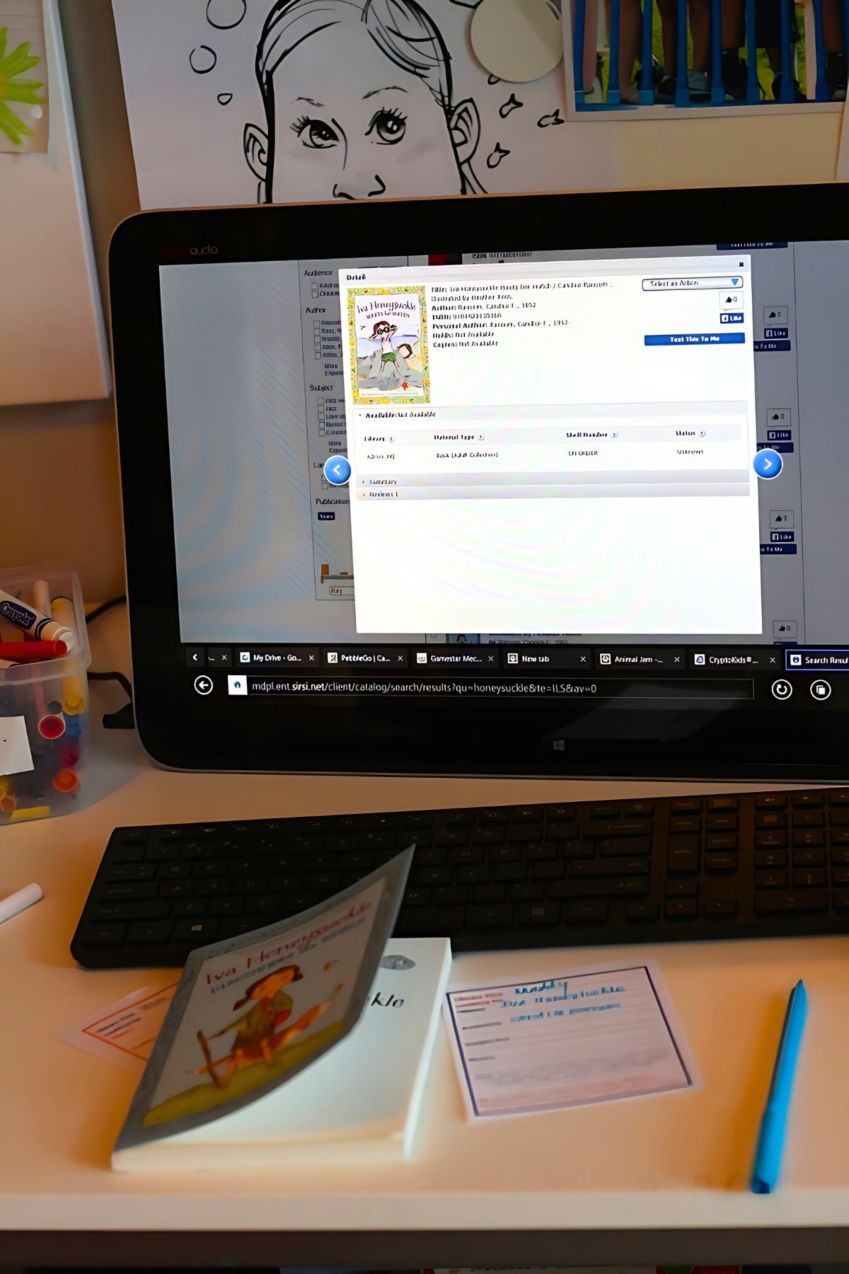 Computer screen with online library catalog on the screen and children's book and library plan sheet on the table