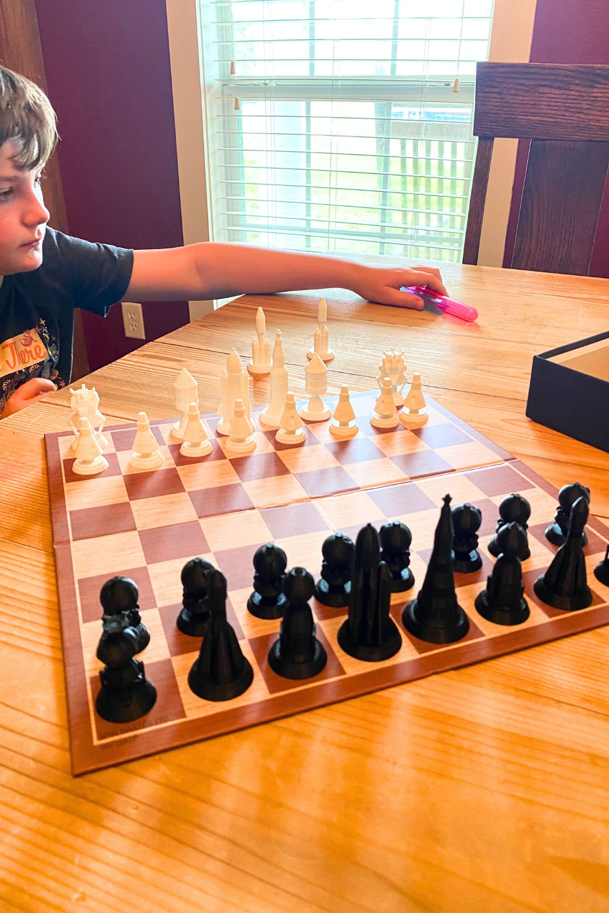 Boy at a wooden table with chess board set up to play