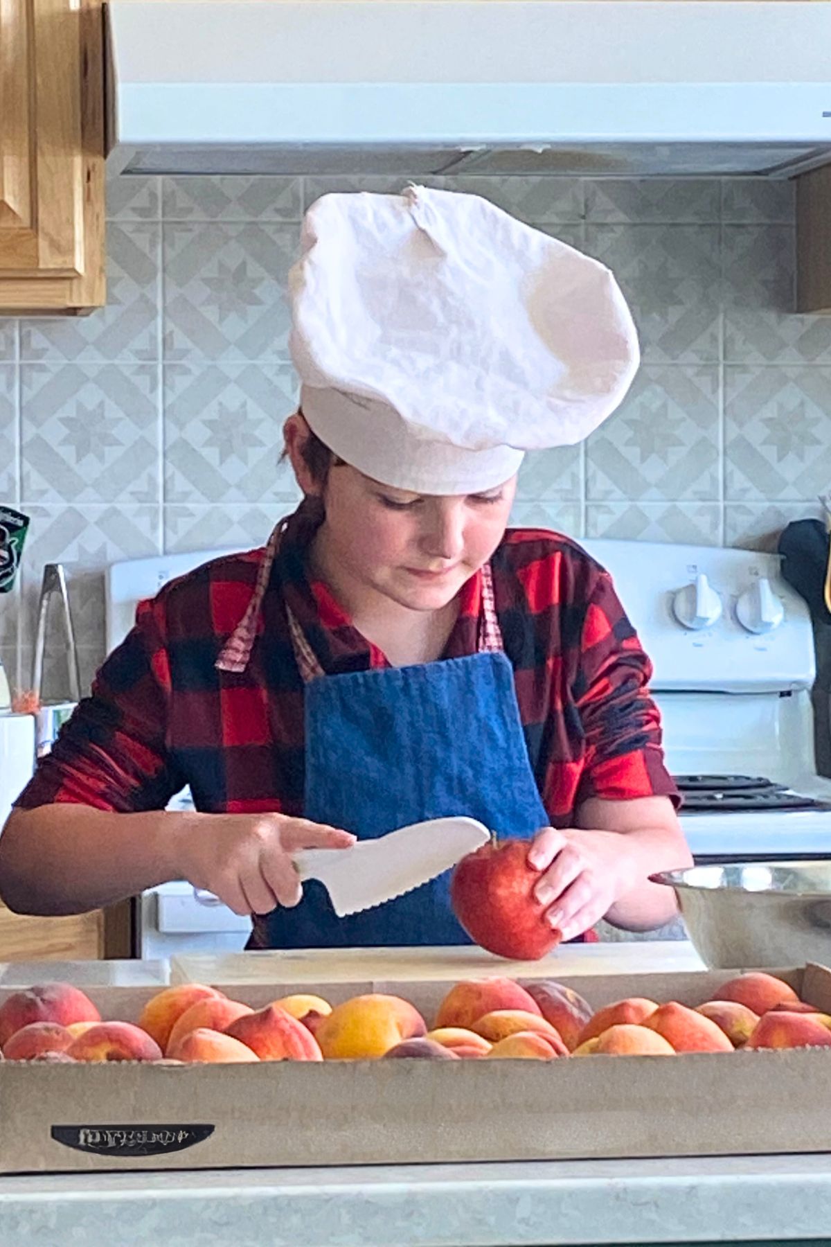 A boy in a chef's hat cutting peaches in the kitchen