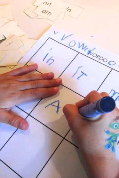 Child's hand writing words on a grid sheet
