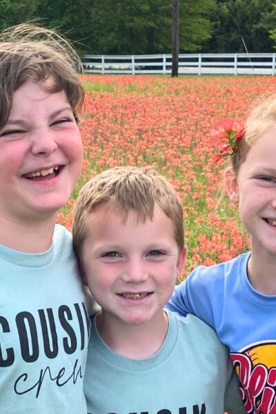 Two boys and a girl wearing blue tee shirts standing a field of Indian Paintbrush wildflowers