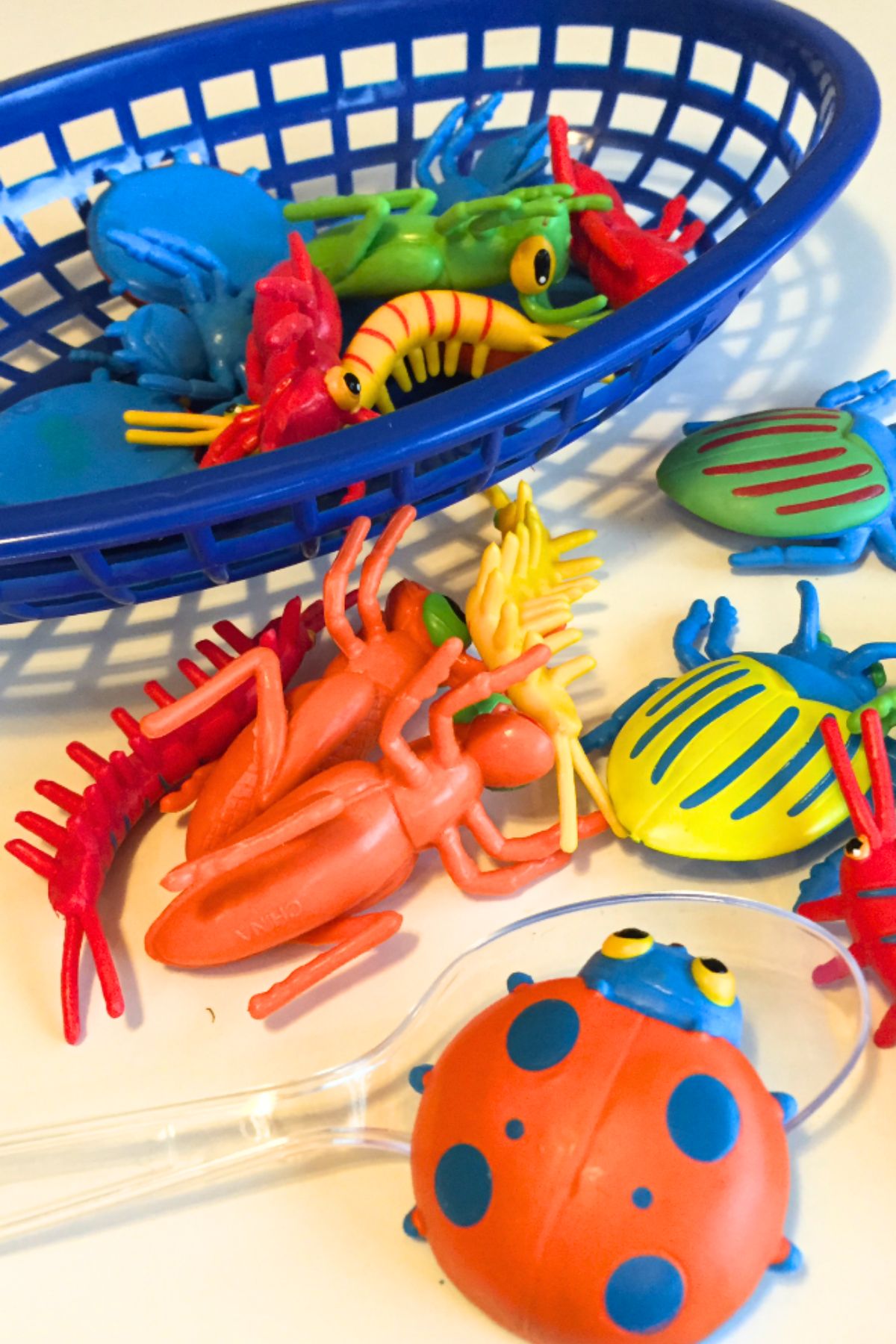 Colorful plastic bugs in a blue plastic basket and a clear plastic spoon