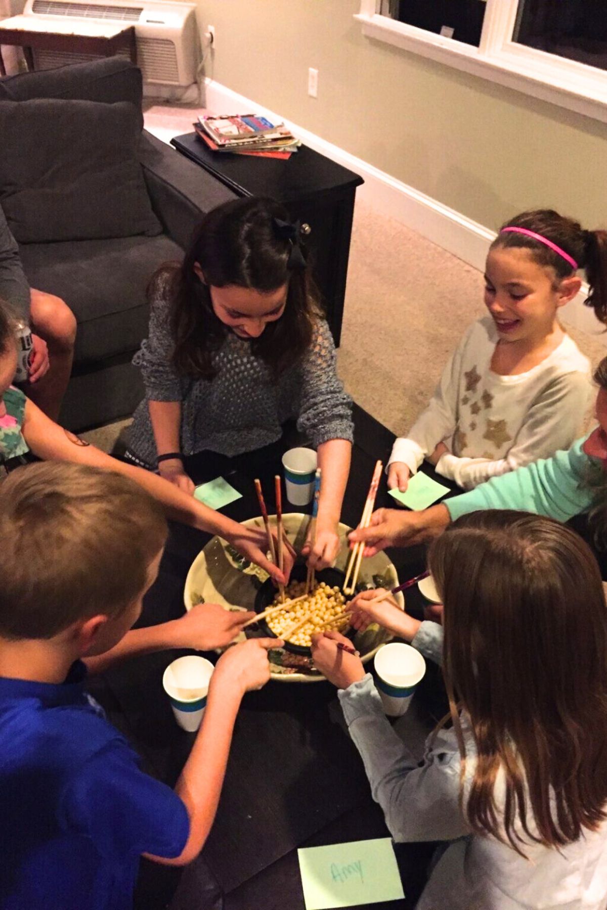 Kids around a table moving Kix cereal from a bowl into cups with chopsticks