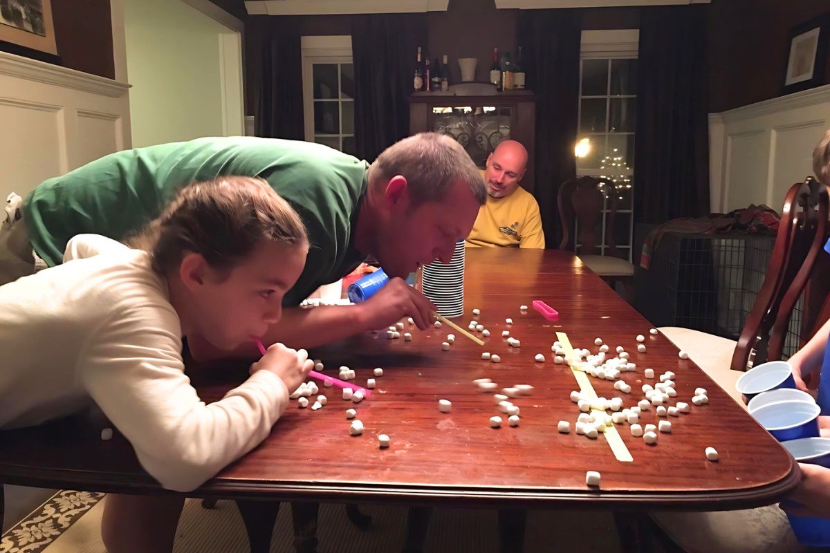 Girl and man racing to blow a marshmallow across a table with a straw