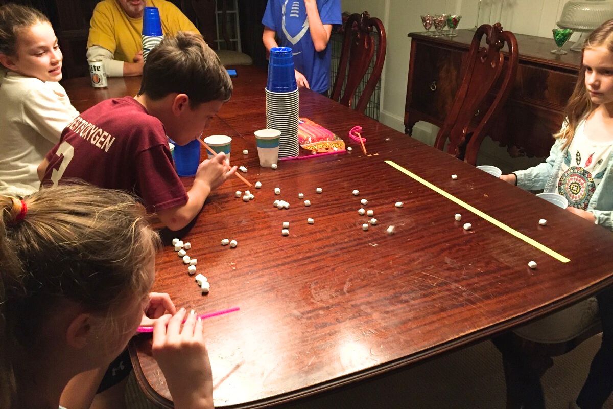 Girl and bow racing to blow marshmallows across a table with a straw