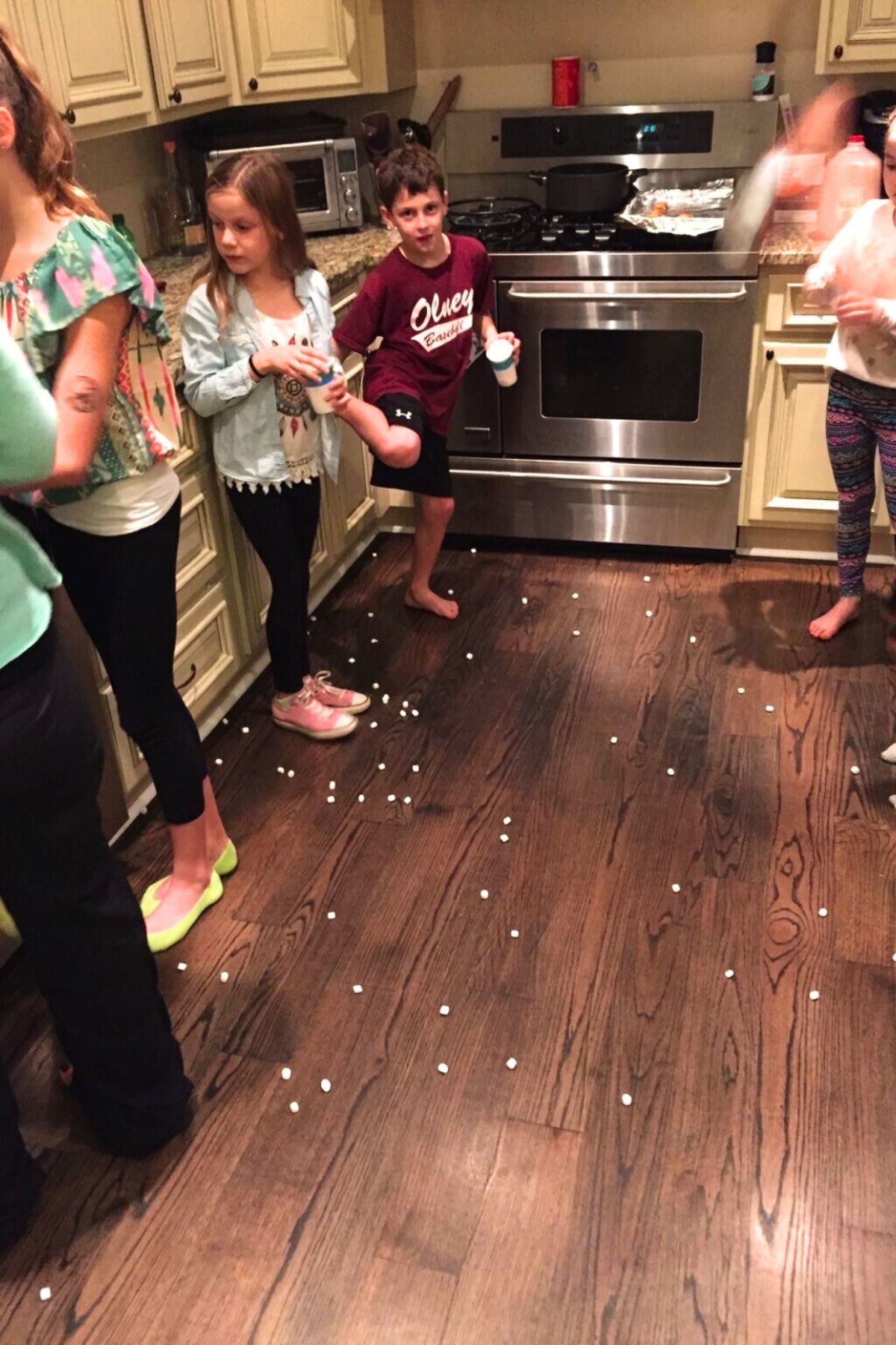 Adults and children standing in lines facing each other in a kitchen. Marshmallows are all over the floor.