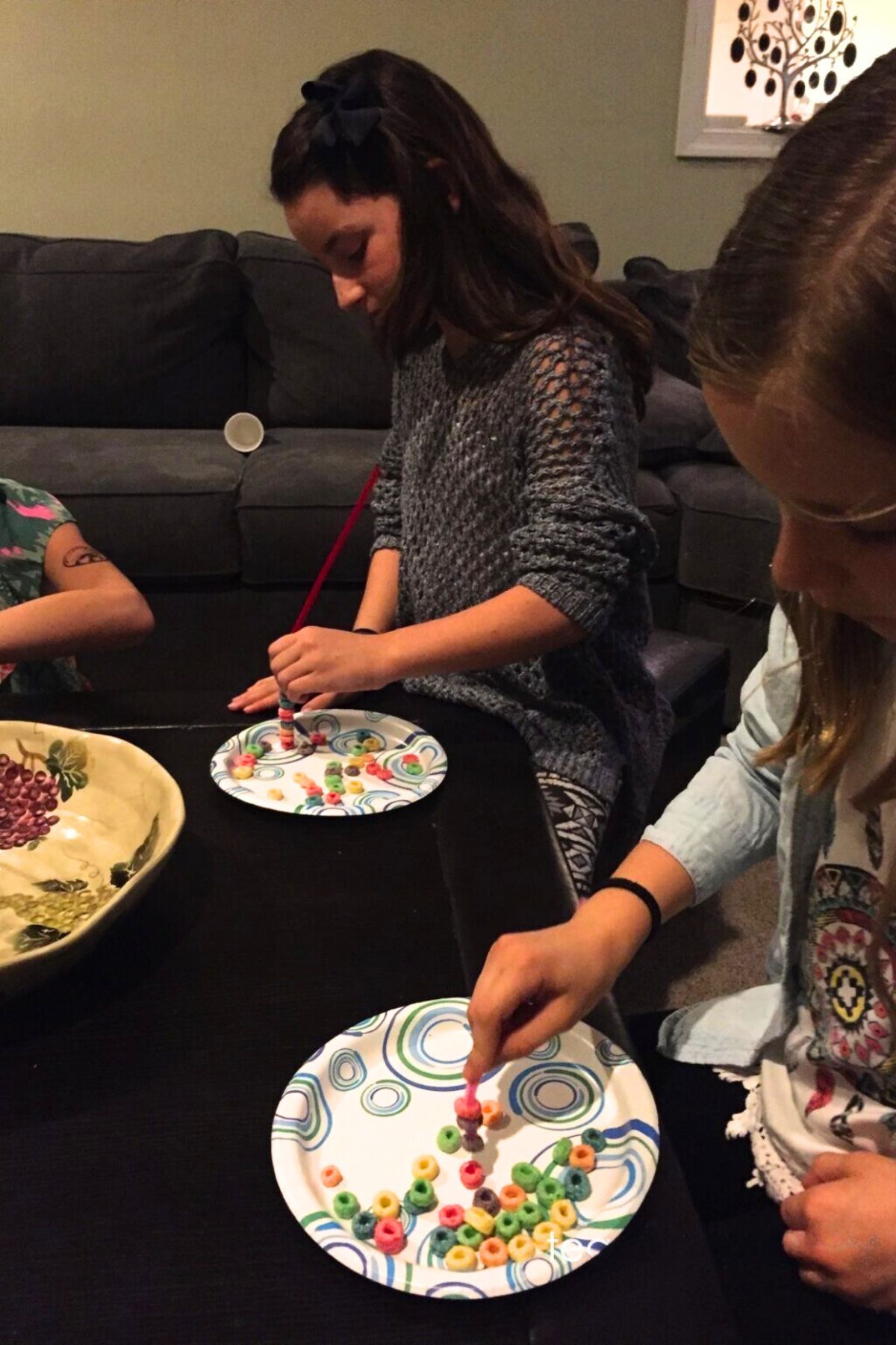 Children around a table stringing fruit loops onto pipe cleaners with one hand