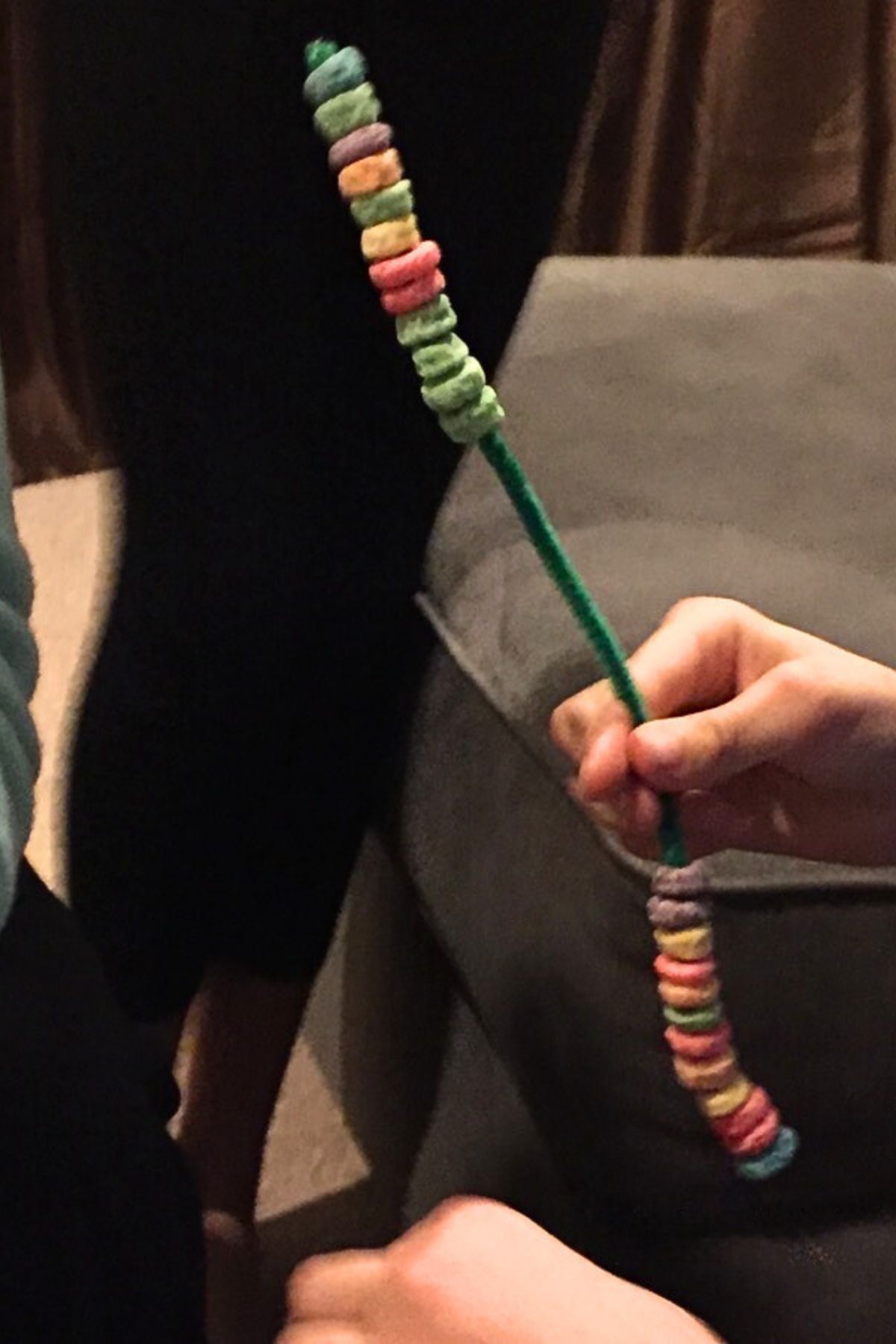 Hand holding a pipe cleaner with fruit loops strung on it
