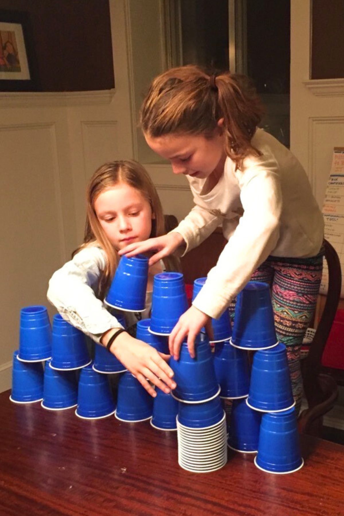 Two girls stacking blue solo cups into a pyramid on a wooden table