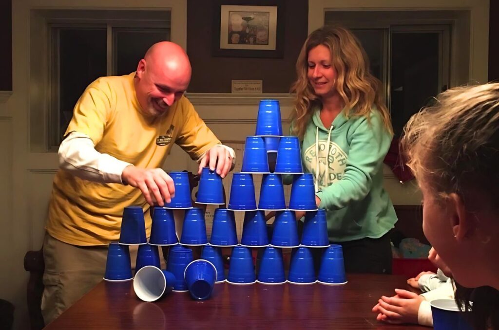 Man and woman stacking blue solo cups into a pyramid on a wooden table