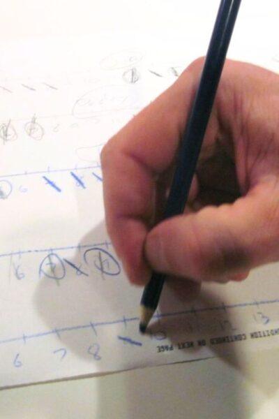 Hand holding a pencil playing a printed strike-it-out game