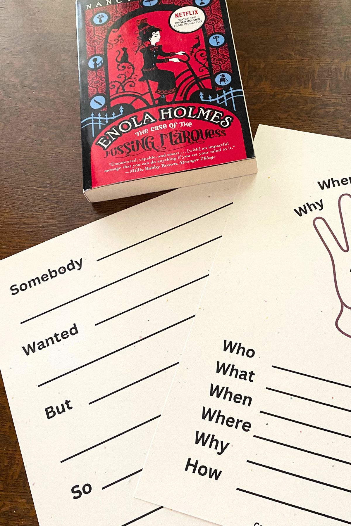 Two worksheets on a table.  One with the outline of a hand and who, what, when, where, why and how and the other with lines to fill out summary points somebody wanted but so...