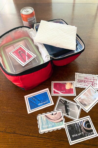 Red soft-sided lunchbox with a white folded paper towel and glass container with several printed wordless riddle notes