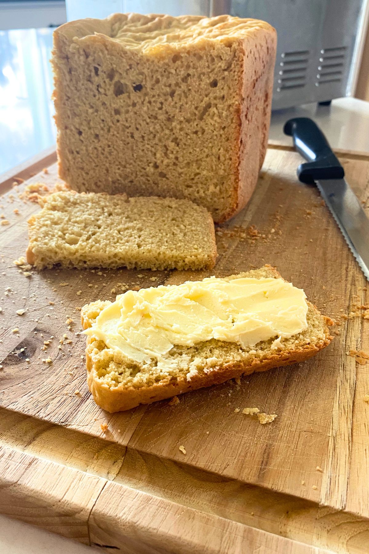 Loaf of homemade bread on a wooden cutting board with one buttered slice in front of it