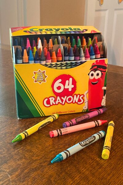 Box of 64 crayons with a few crayons laying in front of it on a wooden table