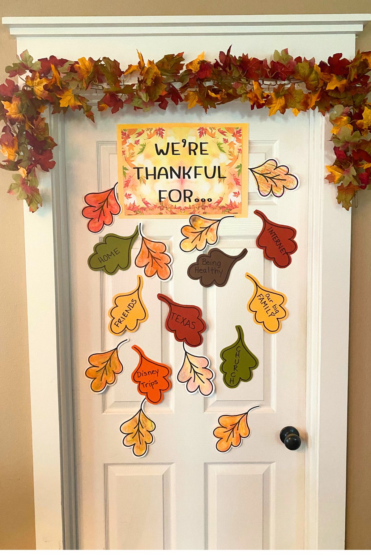 Door with a fall leaf garland across the top and colored leaf taped to the door with blessing written on the leaves
