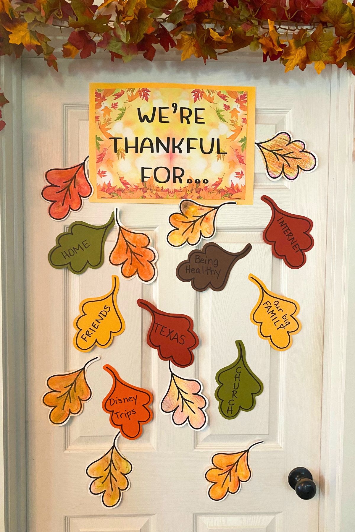 Close up of door with a fall leaf garland across the top and colored leaf taped to the door with blessing written on the leaves