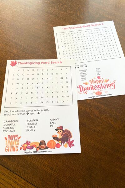 Two Thanksgiving-themed word search puzzles with colorful Thanksgiving images sitting on a wooden table