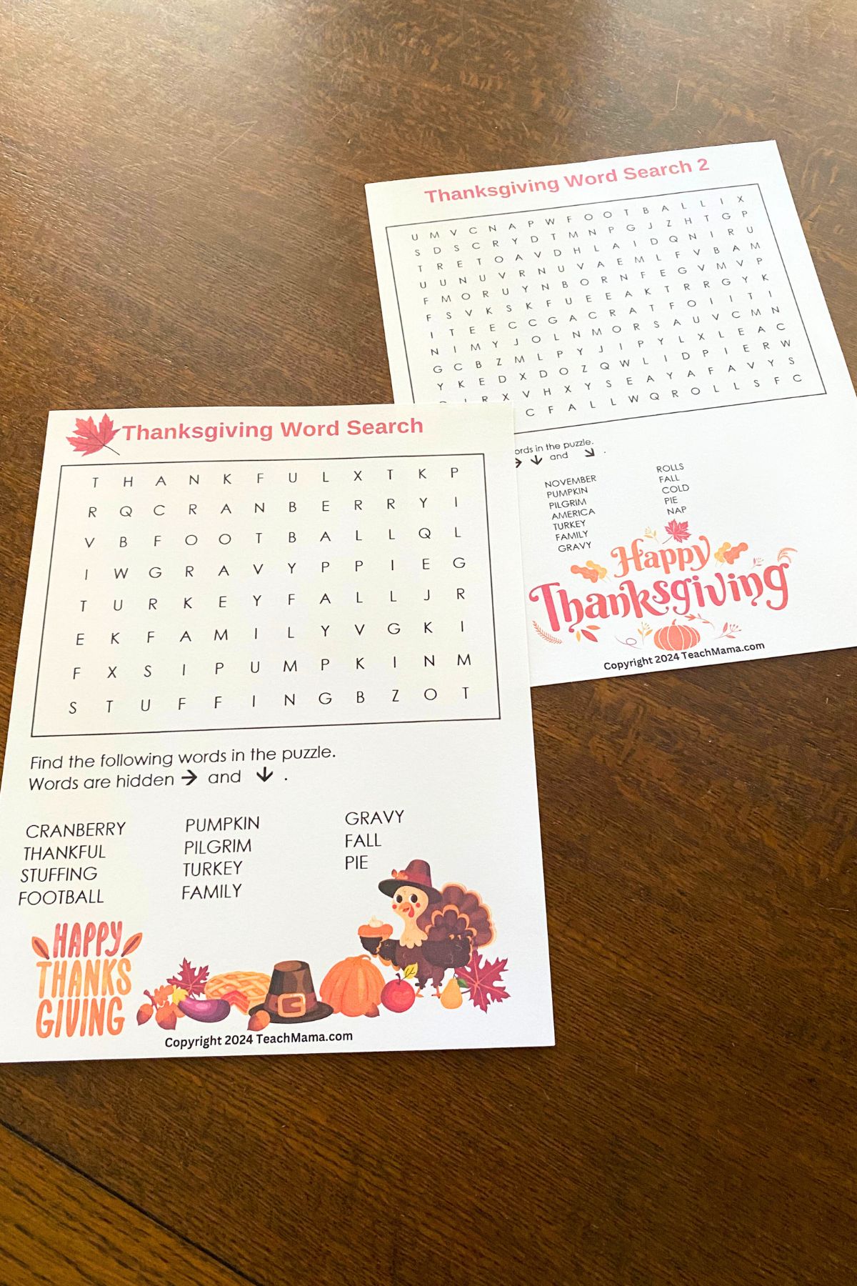 Two Thanksgiving-themed word search puzzles with colorful Thanksgiving images sitting on a wooden table