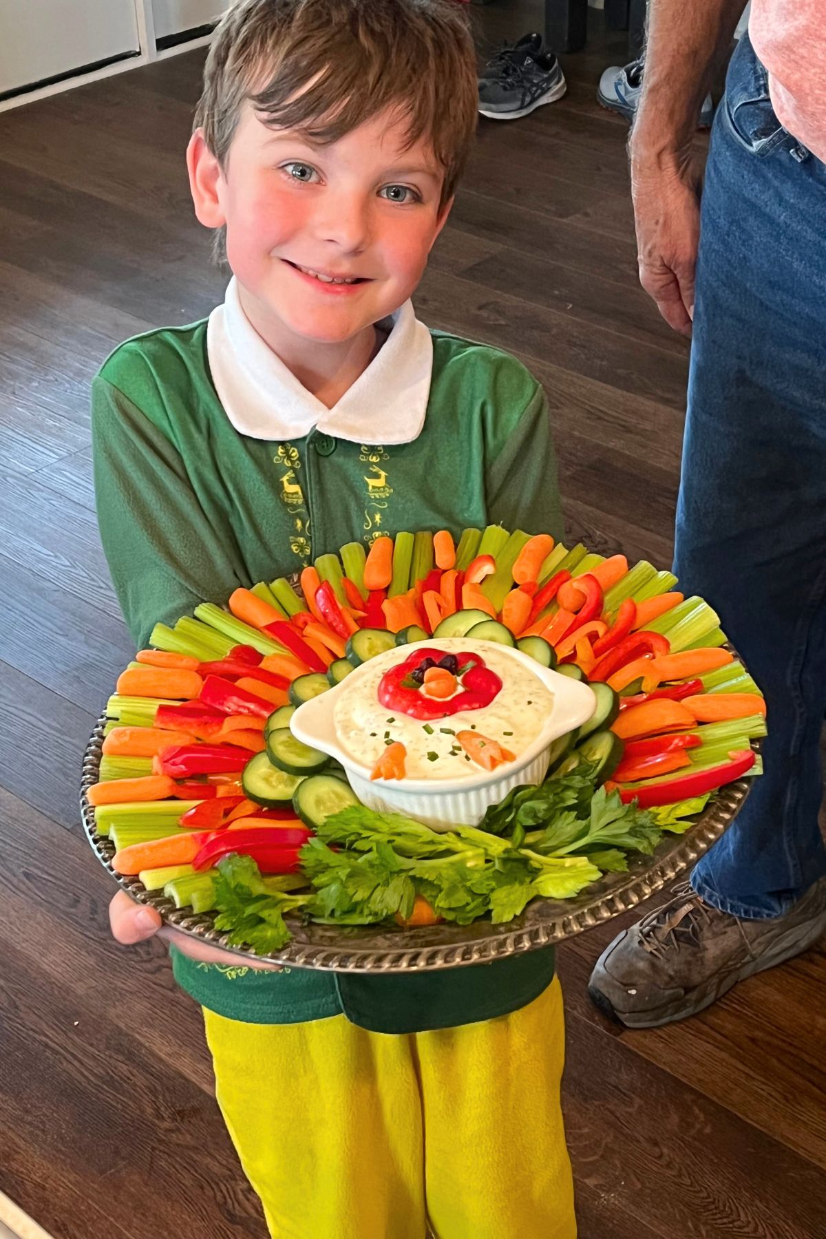 A young boy dressed in an elf costume holding a veggie turkey platter