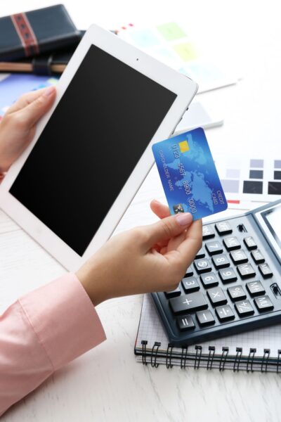 Hands holding a tablet computer and a credit card over papers and a calculator on a desk