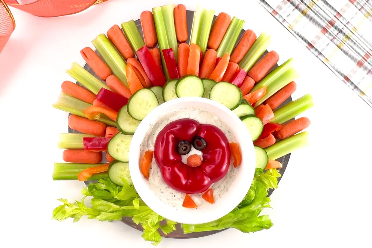 The finished turkey veggie tray made from celery, carrots, bell pepper, cucumbers, surrounding a bowl of ranch dip.