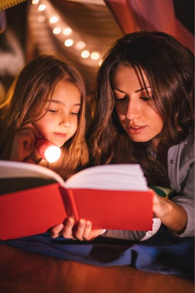 Mom and daughter reading in bed with a flashlight