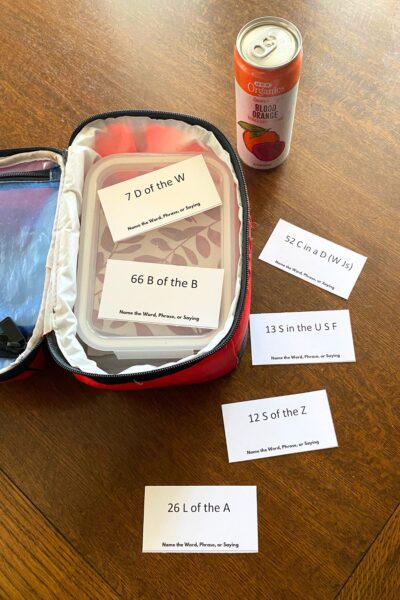 Red soft-sided lunch pail with an orange soda and word puzzle lunchbox notes on a wooden table