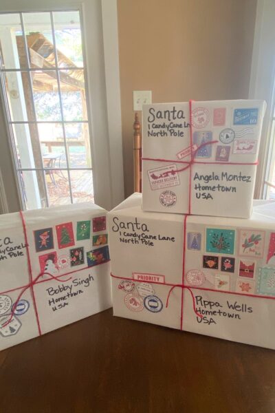 Three boxes wrapped in white paper with red yarn ties and North Pole postal stamps