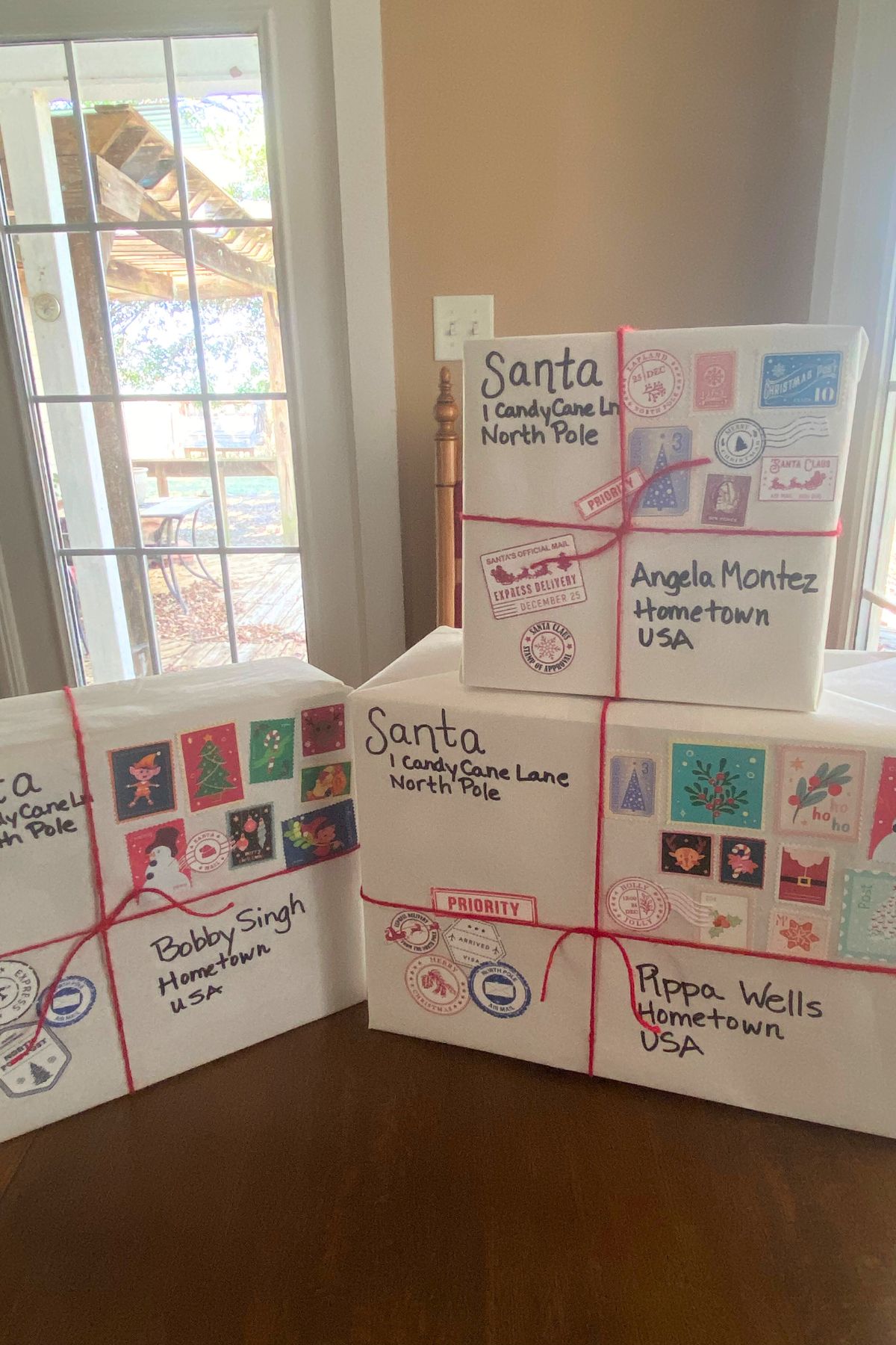 Three boxes wrapped in white paper with red yarn ties and North Pole postal stamps