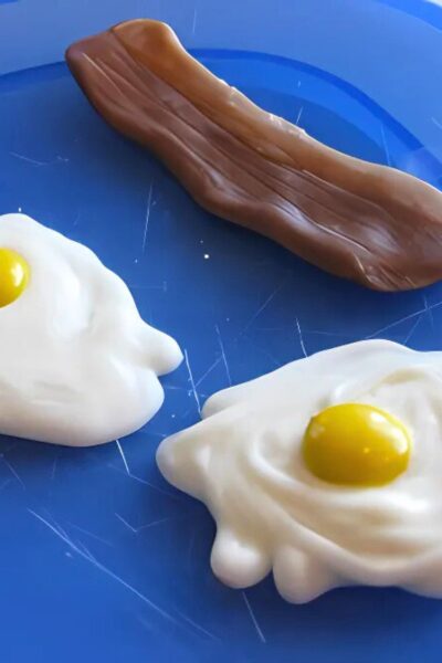 White chocolate "egg" whites with M&M yolks on a blue plate with tootsie roll and caramel "bacon"