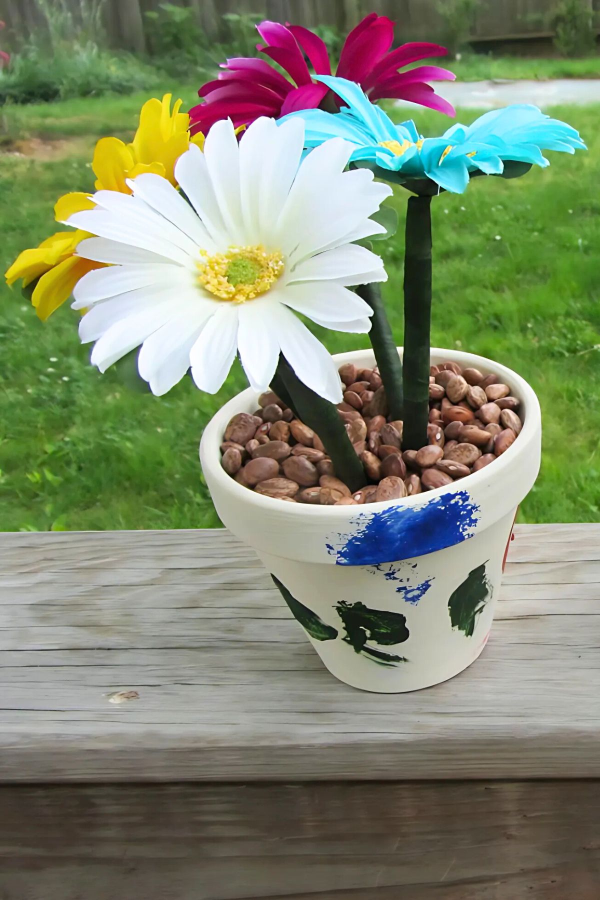 Silk flowers with writing pen stems in a painted flower pot with dry beans as the dirt