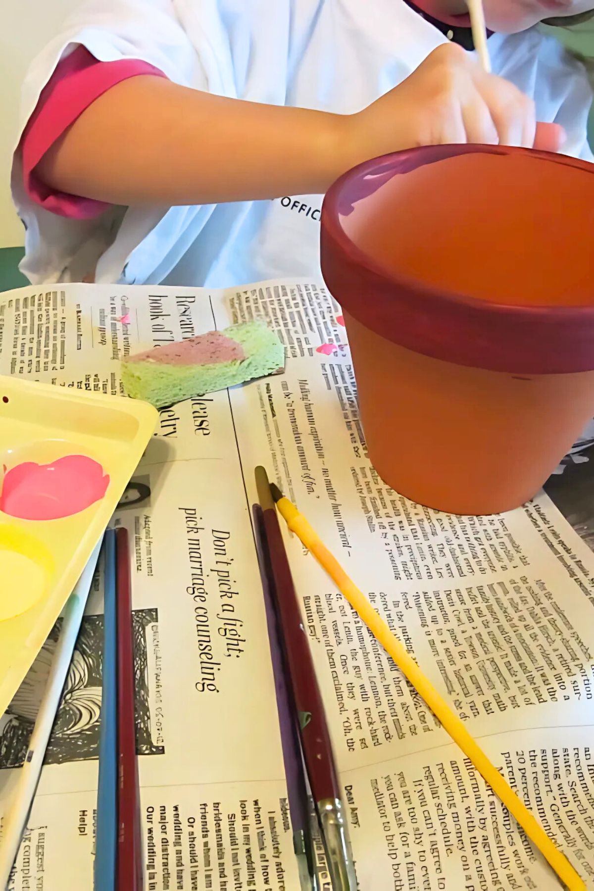 Child painting a terra cotta flower oti with purple point