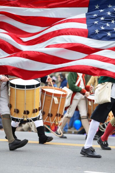 American flag flying with colonial-style parade marchers in the background.