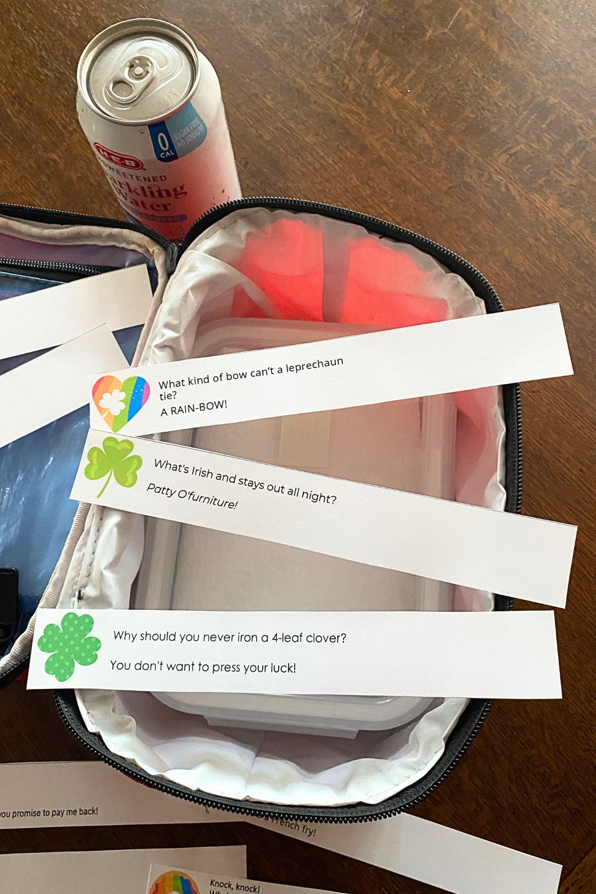 Lunchbox notes cut into strips with a red lunch pail and a canned drink on a wooden table