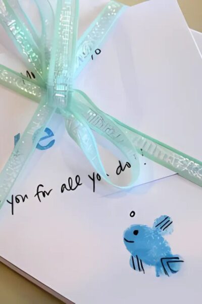 White note card with a green lace ribbon and a blue thumbprint fish