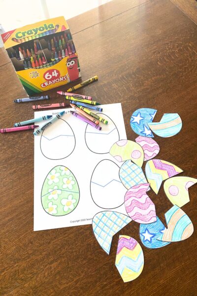 A box of crayons and egg-shaped printed on white card stock decorated with colorful patterns on a wooden table