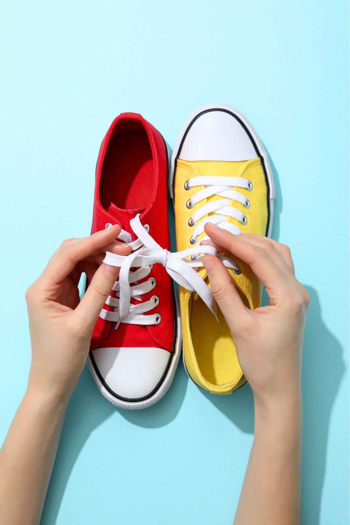 Hand tying the laces of a red tennis shoe and a yellow tennis shoe together