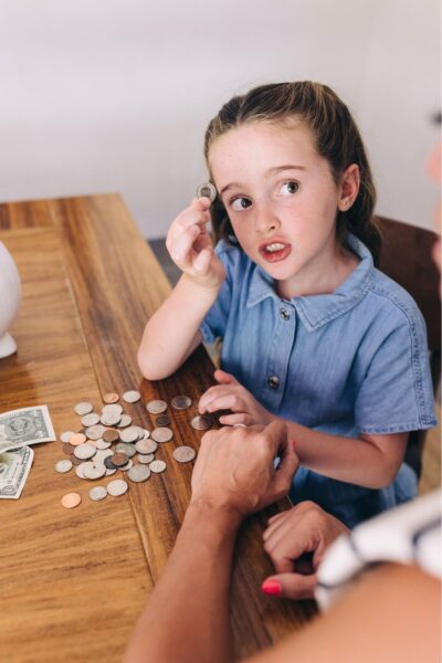 Girl in a blue shirt sitting at a table holding up a coin