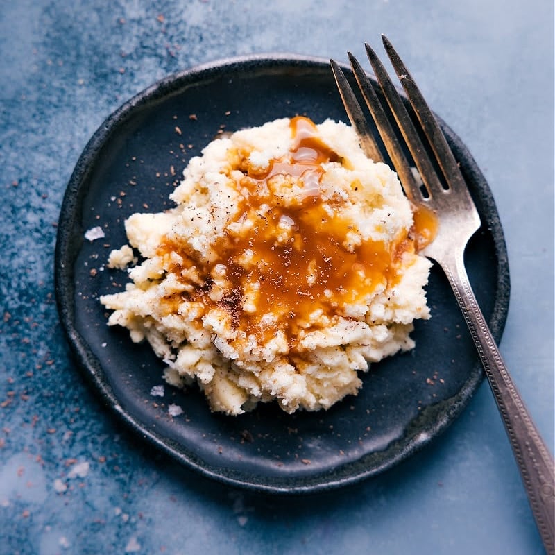 Fake mashed potatoes and gravy on a dark plate with a fork