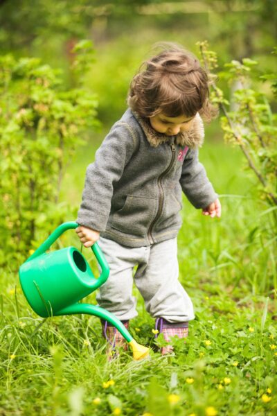 Young child watering plants from a green water can