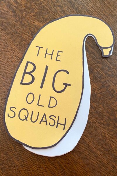 Yellow construction paper cut into the shape of a crookneck squash with The Big Old Squash written in block letters.