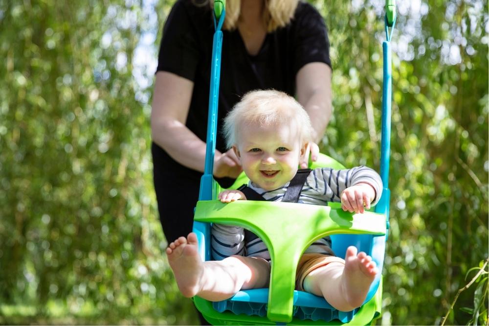 mom pushing her toddler in the swing happily